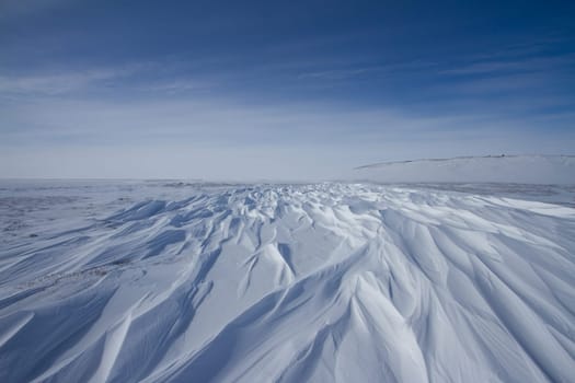 Beautiful patterns of sastrugi, parallel wavelike ridges caused by winds on surface of hard snow, with soft clouds in the sky, near Arviat Nunavut Canada