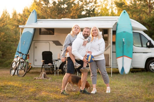 Happy parents with their child playing with a ball near their mobile home in the woods.