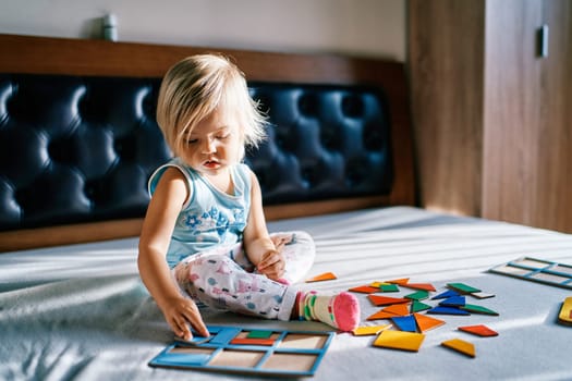Little girl puts together a colorful puzzle on the bed. High quality photo
