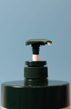 One bottle of green natural shampoo with a dispenser on a blue background, close-up side view. The concept of personal hygiene, cosmetics, beauty.