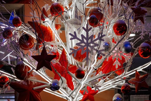 Close-up footage of Christmas Decorations on a Snow-Covered Spruce Tree in dusk, It's snowing, snowflakes are falling, red glass balls and stars, artificial snowflakes, illumination. High quality photo