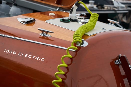 the wooden side of the modern electric elegance motor boat in port of Hercules in Monaco, green electric cable for charging batteries, sunny glare of the sun, glossy surfaces shine in sunny weather. High quality photo