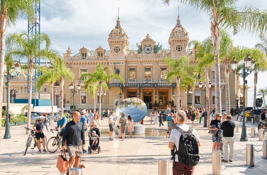 Monaco, Monte-Carlo, 29 September 2022 - Square Casino Monte-Carlo at sunny day, luxury cars, famous Hotel de Paris, wealth life, tourists take pictures of the landmark, pine trees, flowers. High quality photo