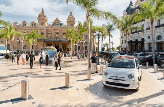 Monaco, Monte-Carlo, 29 September 2022 - Square Casino Monte-Carlo at sunny day, luxury cars, famous Hotel de Paris, wealth life, tourists take pictures of the landmark, pine trees, flowers. High quality photo