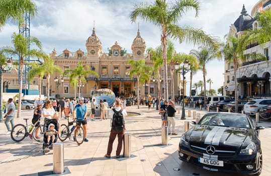 Monaco, Monte-Carlo, 29 September 2022 - Square Casino Monte-Carlo at sunny day, luxury cars, famous Hotel de Paris, wealth life, tourists take pictures of the landmark, pine trees, flowers. High quality photo