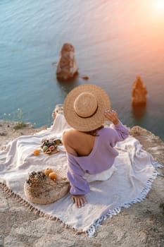woman sea travel. photo of a beautiful woman with long blond hair in a pink shirt and denim shorts and a hat having a picnic on a hill overlooking the sea.