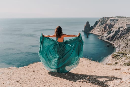 Woman green dress sea. Female dancer posing on a rocky outcrop high above the sea. Girl on the nature on blue sky background. Fashion photo