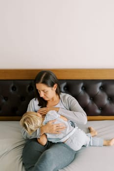 Mom breastfeeds a little girl hugging her in her arms while sitting on the bed. High quality photo