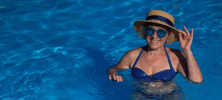 Portrait of an elderly woman in a hat and blue sunglasses swims in the pool