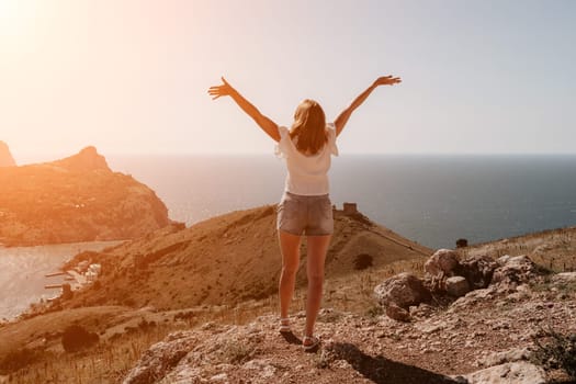 Woman travel sea. Young Happy woman in a long red dress posing on a beach near the sea on background of volcanic rocks, like in Iceland, sharing travel adventure journey