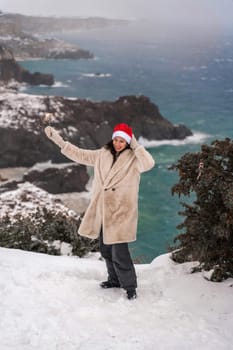 Outdoor winter portrait of happy smiling woman, light faux fur coat holding heart sparkler, posing against sea and snow background.