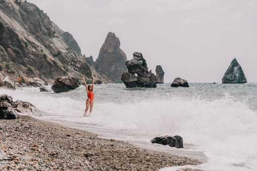 Woman travel sea. Young Happy woman in a long red dress posing on a beach near the sea on background of volcanic rocks, like in Iceland, sharing travel adventure journey