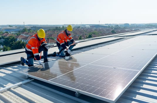Side view of two Caucasian technician workers check and maintenance the solar cell panels on rooftop of the building or factory.