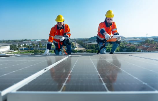 Front view of two Caucasian workers hold document pad and tablet check and maintenance the solar cell panels on rooftop of the building or factory.