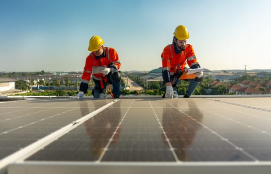 Lower view two Caucasian technician workers hold document pad and tablet check and maintenance the solar panels on rooftop of the building or factory.