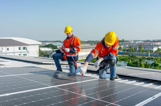 Caucasian technician workers use screwdriver to maintenance and fix the problem of the solar cell panels on rooftop of the building or factory.