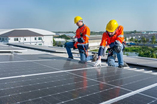 Side view of two Caucasian workers hold document pad and tablet check and maintenance the solar cell panels on rooftop of the building or factory.