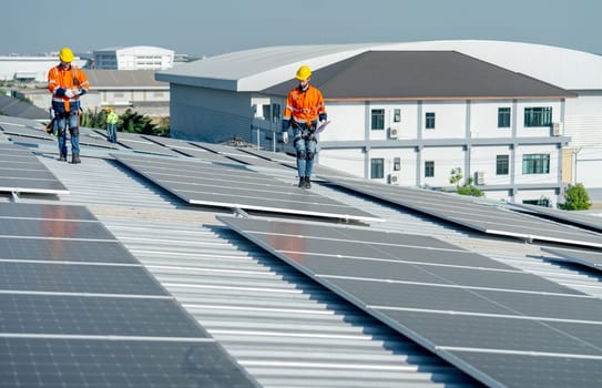 Caucasian technician workers walk together to check and maintenance the solar cell panels on rooftop of the building or factory.