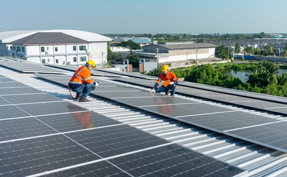 Wide shot two Caucasian technician workers sit on rooftop and discuss abot maintenance the solar cell panels on rooftop of factory or the building. Green and sustainable energy concept.