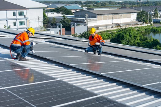 Two Caucasian technician workers sit on rooftop area to check and maintenance the solar cell panels on rooftop of factory or the building. Green and sustainable energy concept.