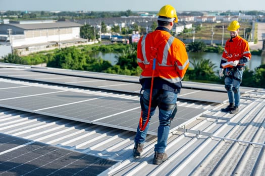 Back of technician worker stand and discuss about installation and maintenance the solar cell panels on rooftop of factory building. Green sustainable energy for good environment concept.