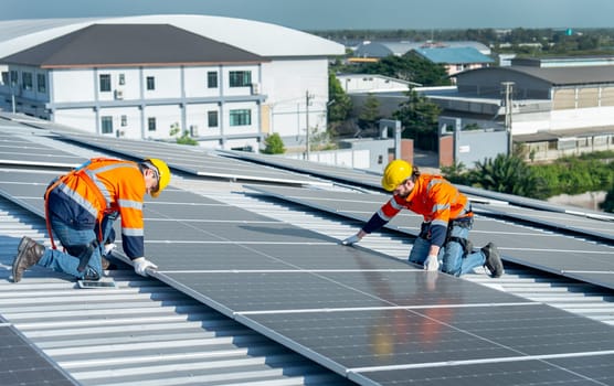 Two Caucasian technician workers work with install the solar cell panels on rooftop of factory or the building. Green and sustainable energy concept.