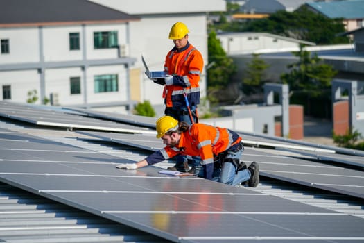 Close up one of technician worker touch to check and maintenance solar cell panels and other co-worker hold laptop to work together on rooftop of factory building.