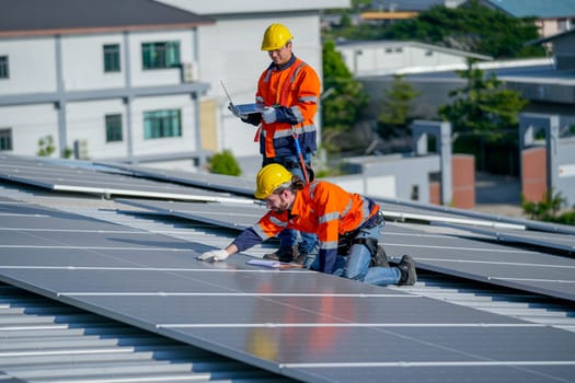 One of technician worker touch to check and maintenance solar cell panels and other co-worker hold laptop to work together on rooftop of factory building.