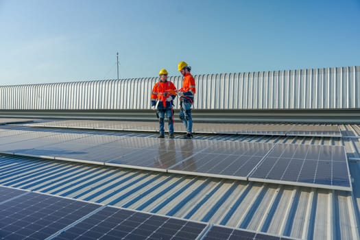 Two Caucasian technician workers stand on rooftop and discuss about the maintenance solar cell panels on rooftop of factory or the building. Green and sustainable energy concept.