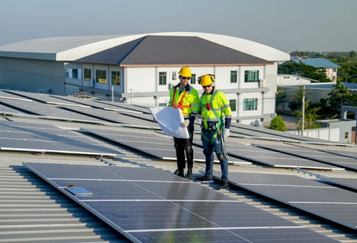 Caucasian technician workers stand with hold construction plan and discuss to co-worker about maintenance solar cell panels on rooftop of factory or the building. Green and sustainable energy concept.