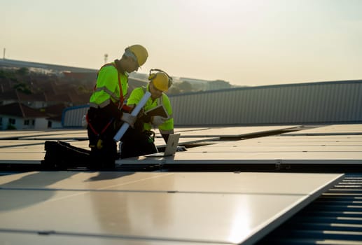 Side view of two Caucasian technician workers look at laptop to check and maintenance solar cell panels on rooftop of factory or the building. Green and sustainable energy concept.