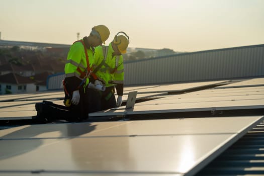 Caucasian technician workers look at laptop to check and maintenance solar cell panels on rooftop of factory or the building. Green and sustainable energy concept.