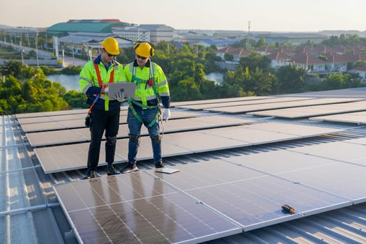 Front view two Caucasian technician workers stand on rooftop and discuss about the maintenance solar cell panels on rooftop of factory or the building. Green and sustainable energy concept.