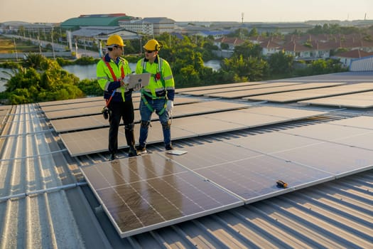 Two Caucasian technician workers stand on rooftop and discuss about the maintenance solar cell panels on rooftop of factory or the building. Green and sustainable energy concept.