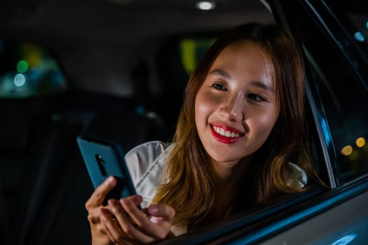 Happy beautiful woman texting smartphone sitting car back seat in urban, Asian businesswoman working late commuting from office in Taxi backseat with mobile phone in city at night after late work