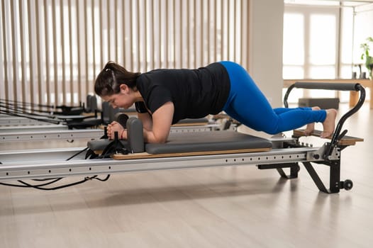 Overweight caucasian woman doing pilates exercises on a reformer