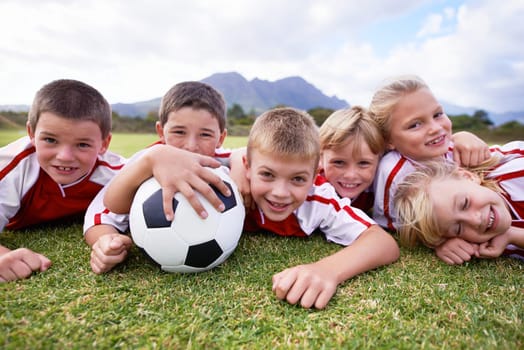 Children, soccer ball and relax on green grass or field for outdoor match, game. or team sports. Group of kids, friends or football players smile lying together for competition on stadium in nature.