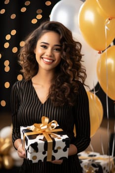 People, joy, fun and happiness concept. happy mixed race birthday woman holding with gift box, gold and black balloons in the background. AI Generated