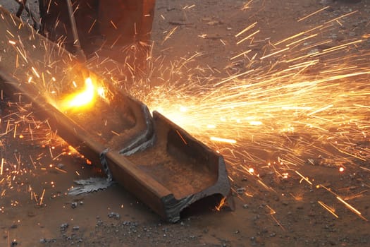 A worker recycles an old, rusty iron rail using an autogen, cutting metal with a gas torch, close-up.