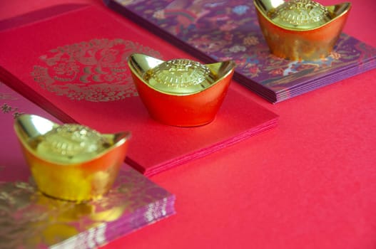 Red envelope and golden ingots on red cover background with Chinese New Year wishes.