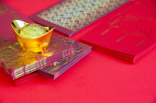 Red envelope and golden ingots on red cover background with Chinese New Year wishes.