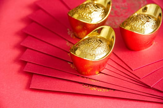 Red envelope and golden ingots on red cover background with Chinese New Year wishes.