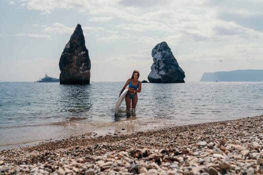 Close up shot of beautiful young caucasian woman with black hair and freckles looking at camera and smiling. Cute woman portrait in a pink bikini posing on a volcanic rock high above the sea