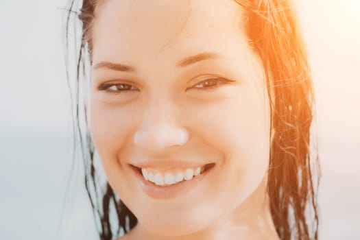 Close up shot of beautiful young caucasian woman with black hair and freckles looking at camera and smiling. Cute woman portrait in a pink bikini posing on a volcanic rock high above the sea