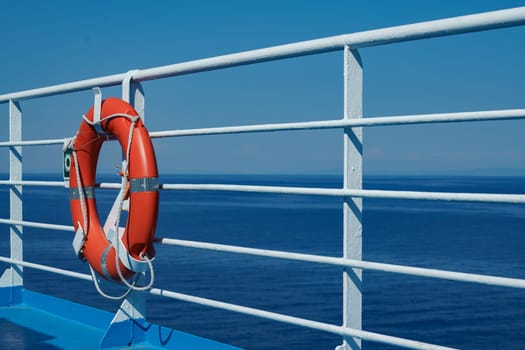 a red lifebuoy hangs on board a ferry cruise ship against the backdrop of a blue sea and a cloudless sky. High quality photo