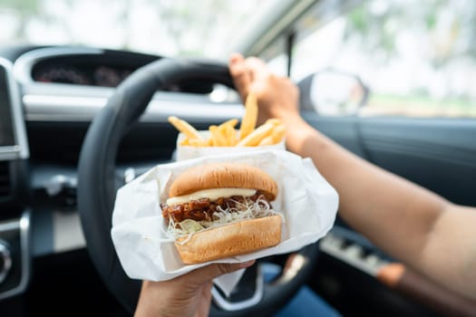 Asian lady holding hamburger and French fries to eat in car, dangerous and risk an accident.