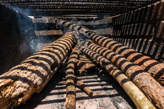 Barbecue wood logs giving smoke and about to catch fire. Striped shadow from grill grate on a bright sunny day. Concept of barbecue in the nature