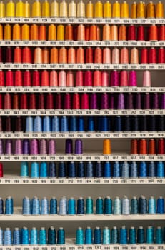 Multi-colored spools of thread on the shelf. Vertical shot