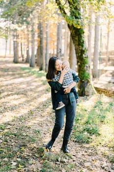 Smiling mother stands in the forest hugging a little girl in her arms. High quality photo