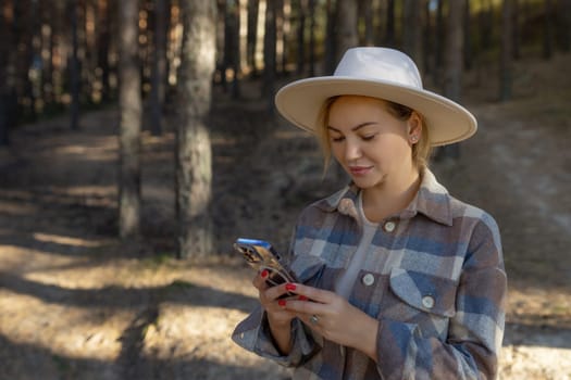 Autumn portrait of a smiling woman holding a phone against the background of the forest Happy girl using a mobile phone alone in the forest in nature in autumn. Copy space.